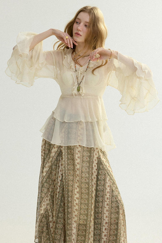 Woman wearing a layered outfit with a sheer top and patterned skirt on a light background