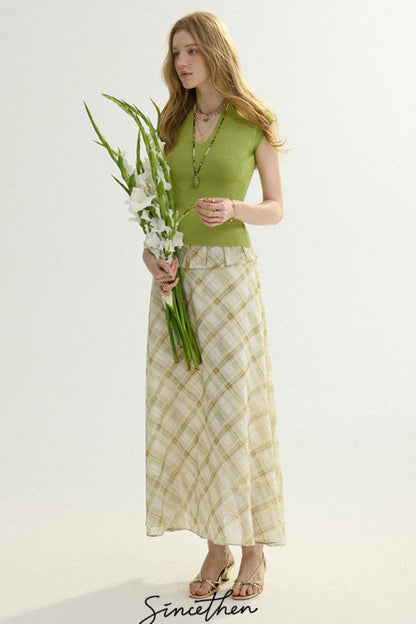 Woman in a green top and patterned skirt holding flowers against a white background