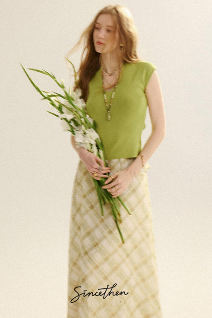 Woman holding flowers wearing a green top and patterned skirt on a light background
