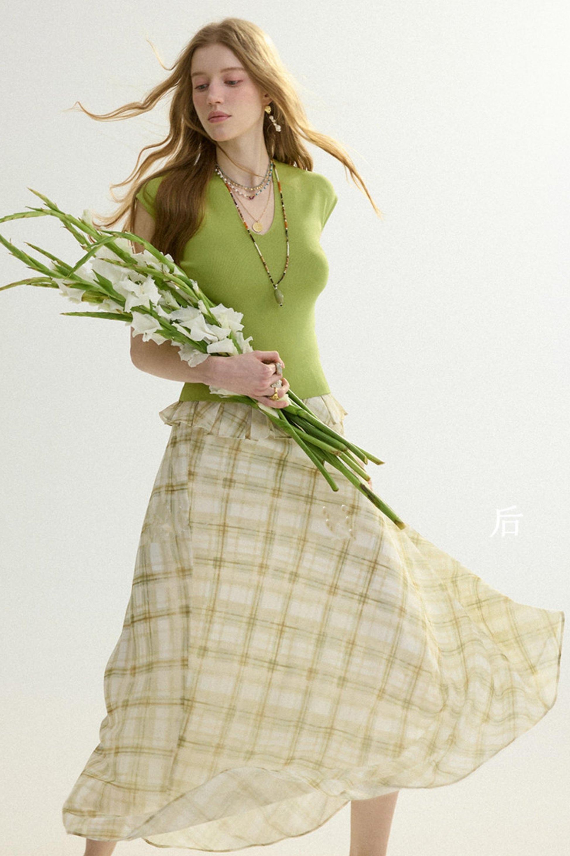 Woman in a green top and plaid skirt holding flowers against a white background