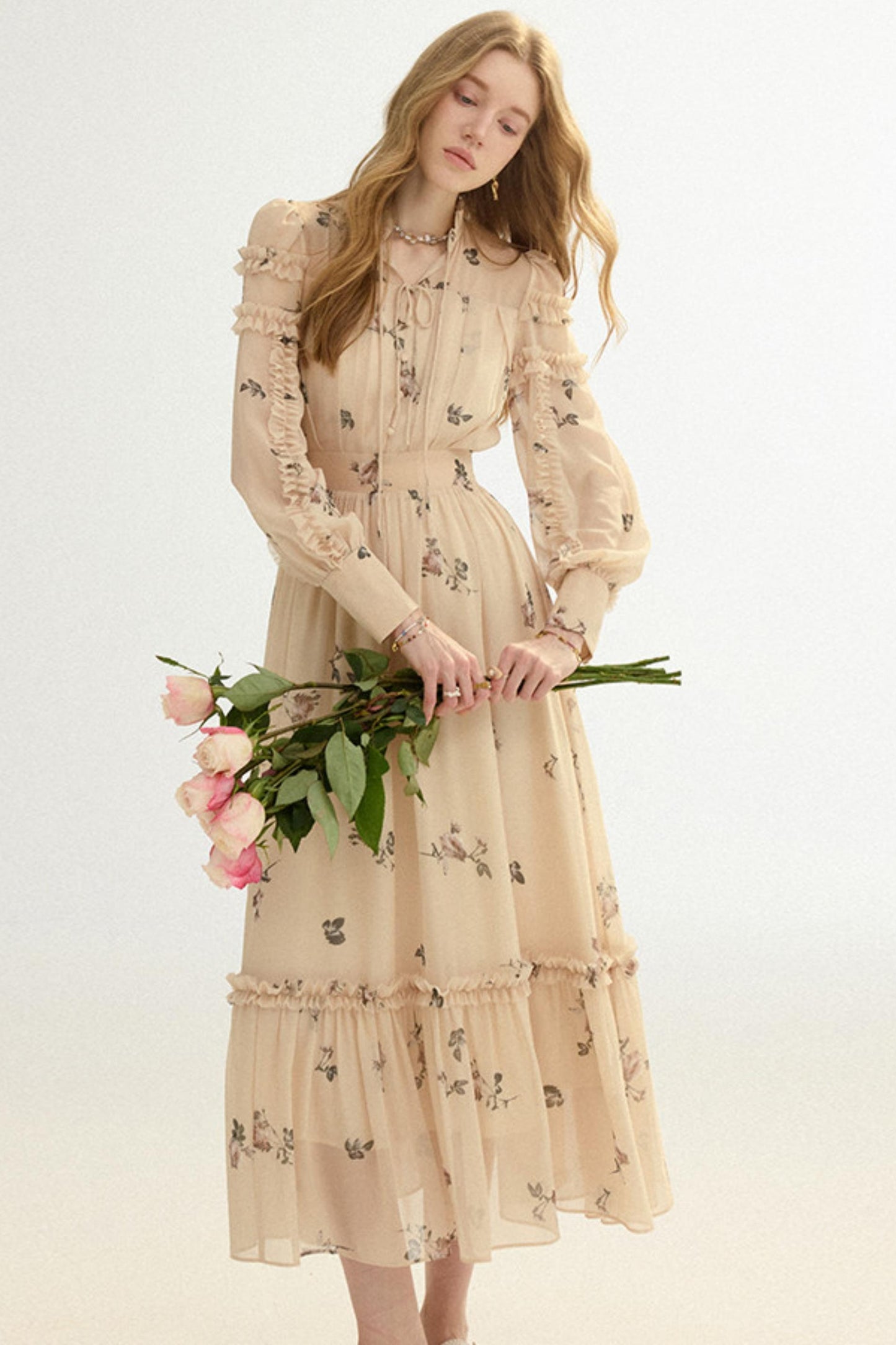 Woman in a beige floral dress holding flowers against a white background