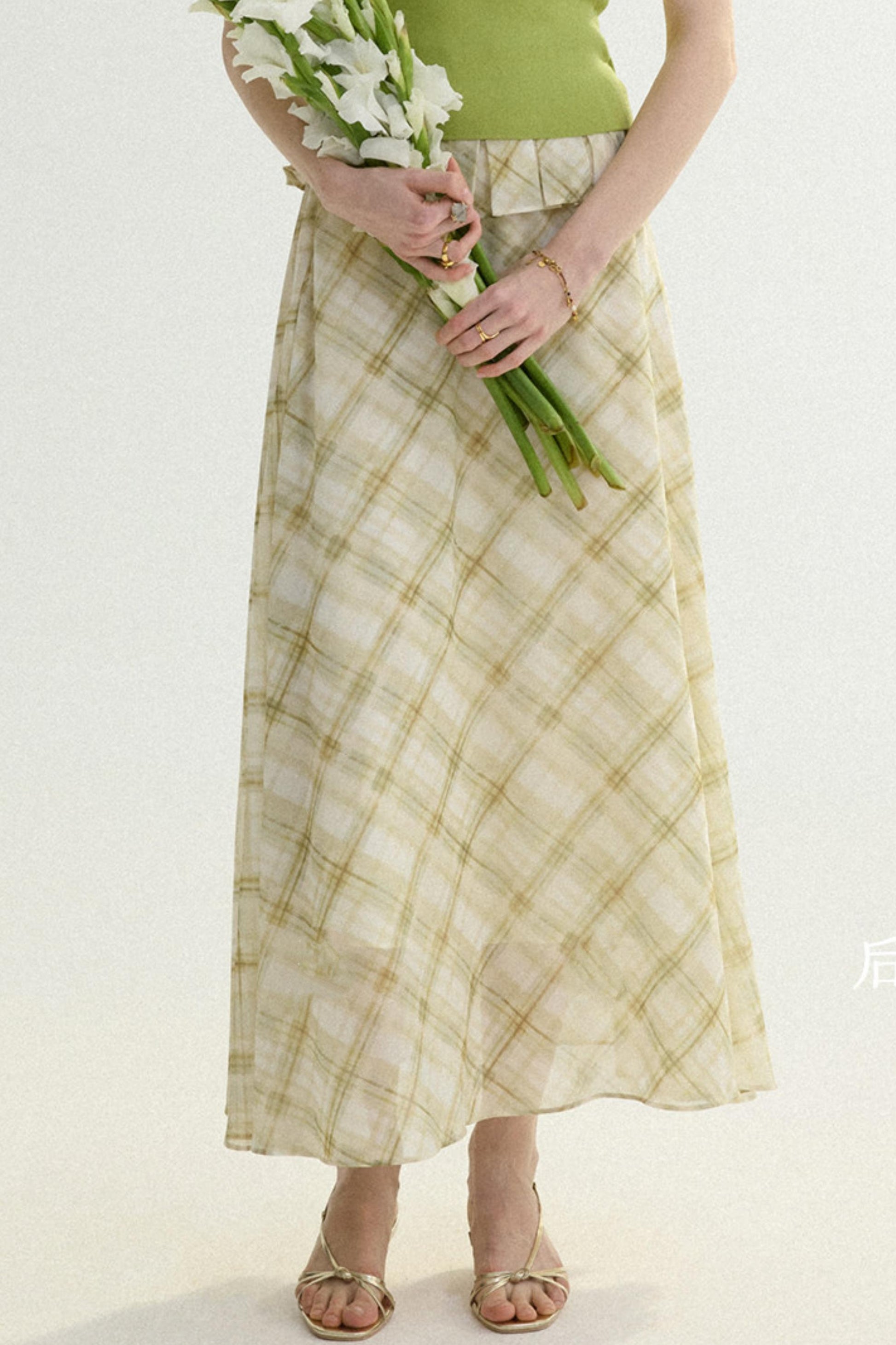 Person wearing a green top and plaid skirt holding white flowers on a white background