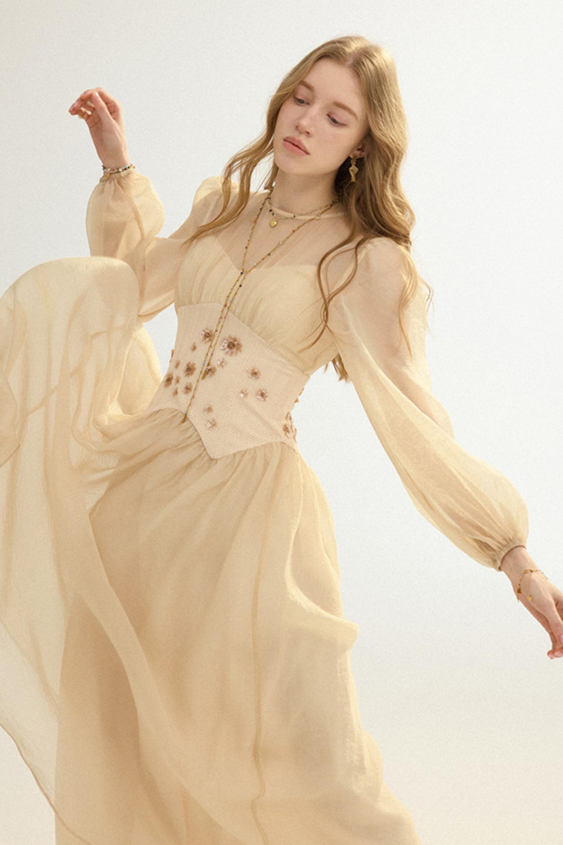 Woman wearing a beige long-sleeve dress with floral details on a light background