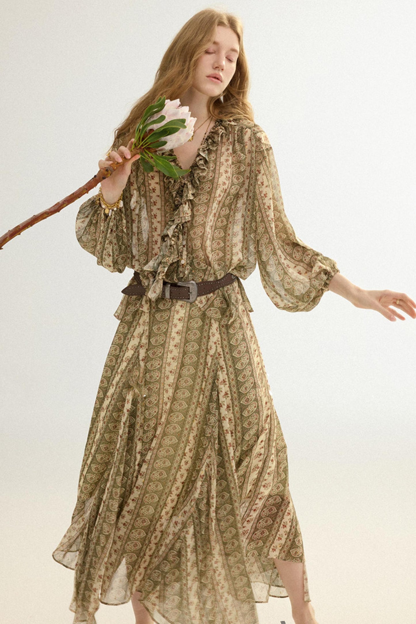 Woman wearing a patterned dress holding a flower against a white background