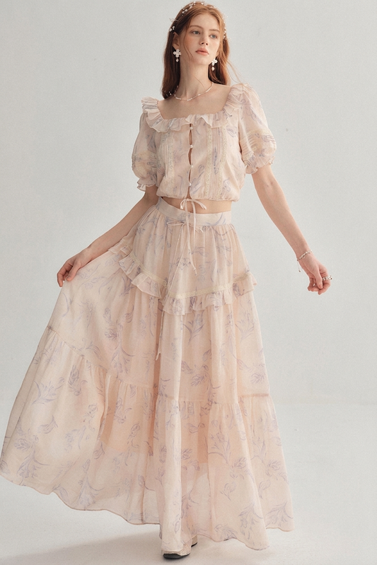 A woman modeling a light blush pink two-piece outfit with a delicate floral print.