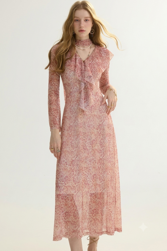 A woman modeling a long-sleeve midi dress with a ruffled high neck and a pink floral pattern, set against a plain light background.